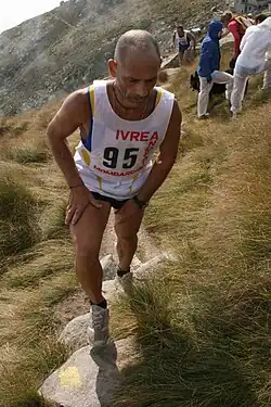 Un coureur montant un sentier, les mains posées sur les cuisses.