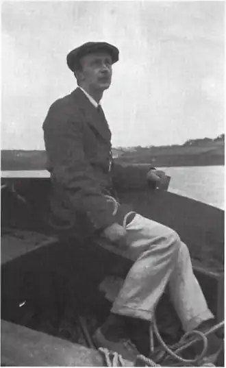  assis sur l'extrémité avant d'une barque, un homme coiffé d'un béret regarde au loin, cordes à la main.