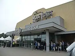 Devanture d'un bâtiment jaune et gris, à l'entrée duquel est écrit en relief « The Making of Harry Potter, Warner Bros Studio Tour ».