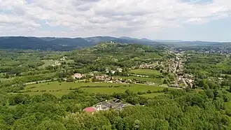 Une colline boisée derrière laquelle s'étendent des montagnes.
