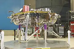 Photo de l'atterrisseur InSight avec son train d'atterrissage déployé posé sur le sol d'une salle blanche.