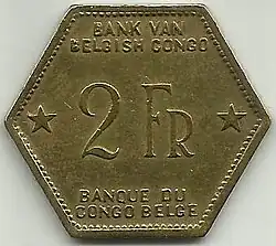 Une pièce jaune hexagonale portant les mentions « Bank van Belgisch Congo. 2 Fr. Banque du Congo belge. »