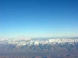 Vue aérienne, crête dominée par un cône volcanique, tous deux enneigés, sous un grand ciel bleu.