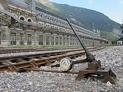 Vue d’un aiguillage en premier plan, avec une gare ferroviaire en arrière plan.