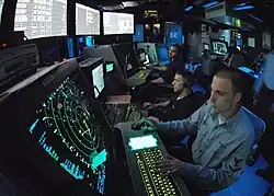 Membres d'équipage en train de surveiller des écrans radars lumineux dans un environnement sombre.