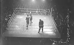 Photographie en noir et blanc prise de haut d'un combat de boxe.