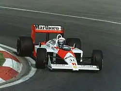 Photo d'Alain Prost au volant d'une McLaren MP4/4 en train d'engager un virage serré.