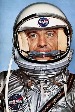 Photographie en couleur de Shepard avec un casque sur la tête, visière ouverte, et sa combinaison argentée.