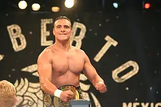 Un homme brun torse nu avec une ceinture de champion de catch.