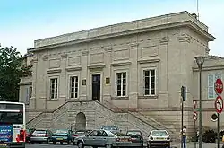 Photo couleur d'un bâtiment d'architecture classique à un seul étage et entrée surélevée desservie par un perron. Une corniche au sommet des murs masque la toiture.