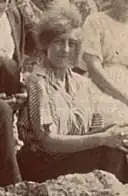 photo sépia d'une jeune femme assise sur un rocher, en chemisette, les cheveux volant au vent