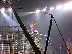 un catcheur en combinaison bleu sur le toit d'une cage.