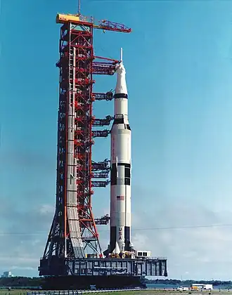 Le lanceur Saturn V sur sa table de lancement. Une tour de service permet d'accéder jusqu'à la dernière minute aux différentes parties du lanceur et d'alimenter en ergols le lanceur.
