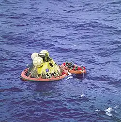 Photographie en couleur de la capsule d'Apollo 11 flottant en mer lors de la récupération des astronautes.