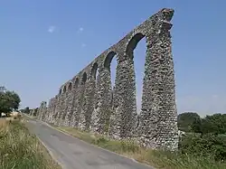 Vue des vestiges d'un aqueduc antique longeant une route.
