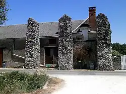 Vue du pignon d'une ferme partiellement engagé entre deux piles ruinées d'un aqueduc.