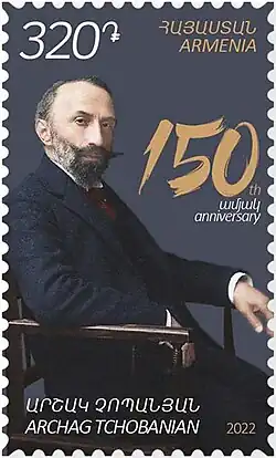 Timbre en couleur représentant, assis, un homme barbu portant un costume et une cravate.