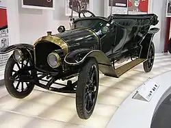 Une voiture ancienne dans un musée, toit découvert, haute calandre, grands phares ronds.