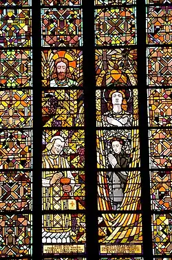 Élément de vitrail. Quatre personnages sont présents. À gauche, un homme barbu au-dessus d'un vieux prêtre. À droite, un jeune homme avec une longue chevelure au-dessus d'une jeune femme en armure.