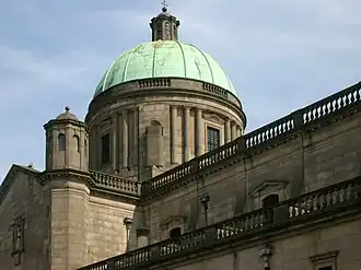 Photo en contre-plongée d'un bâtiment en briques ocres avec une tour surmontée d'un dôme couleur vert-de-gris, lui-même coiffé d'un édicule