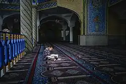 Assis en tailleur dans un rayon de lumière un jeune garçon lit un livre qu'il tient dans ses jambes. Le reste du lieu est vide, est la pièce, ses tapis, murs, piliers, couloirs, voutes, sont dans une quasi obscurité.