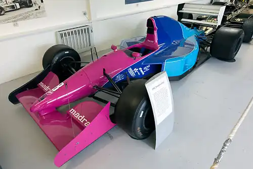 Photo d'une monoplace de Formule 1 de 1992 au nez rose, à l'arrière bleu et à l'aileron arrière blanc, dans un musée