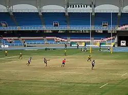 Un joueur de rugby frappe au pied dans le ballon, d'autres courent dans la même direction que le ballon.