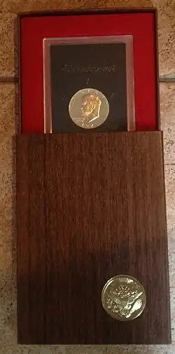 Coffret en bois, partiellement ouvert, sur lequel se trouve un sceau et contenant un cadre avec une pièce de monnaie et l'inscription Eisenhower.