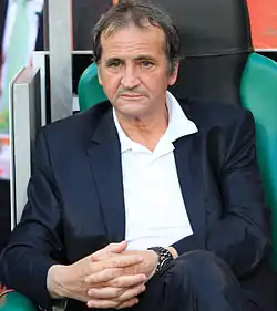 Photographie en couleur d’un homme assis de face les mains croisées.