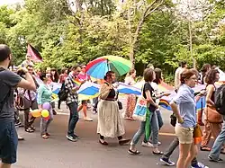 Photographie de la marche des fiertés 2014 à Bucarest. Une partie du cortège de manifestants et manifestantes, portant un immense drapeau arc-en-ciel.