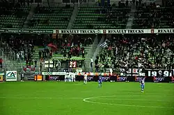 Photo montrant des personnes dans une tribune, derrière des joueurs de football en premier plan