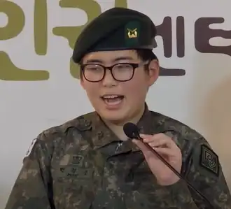 Femme asiatique portant un uniforme militaire et des lunettes, parlant dans un microphone