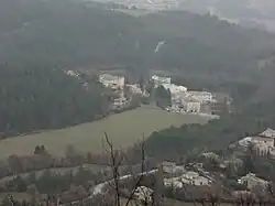 En plongée : quelques bâtiments modernes proches d'un château moderne, à la jonction d'un pré et de forêts, au fond d'une vallée. Les pavillons résidentiels voisins occupent le quart inférieur droit de la photo.
