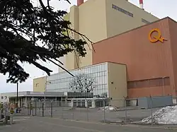 Des portes vitrées à l'entrée d'un bâtiment de couleur brune. Un logo jaune formé d'un Q et d'un éclair orne la façade.