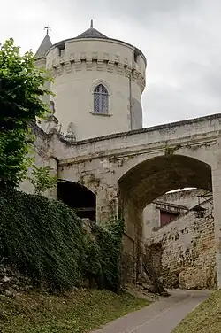 Photographie en couleurs d'une tour cylindrique couverte d'ardoises en arrière-plan d'un pont enjambant une rue encaissée.