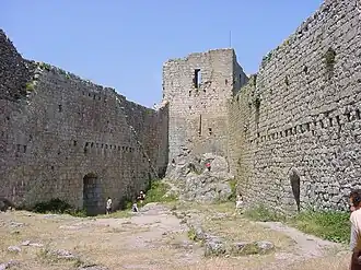 photo couleur montrant un château vu de la cour intérieure. Une tour, au fond, est reliée à deux murailles percées de trous montrant des emplacements de poutre anciens.