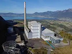 Bâtiment rectangulaire et gris devant un panorama d'un lac.