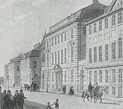 Photographie en noir et blanc d'une gravure représentant un bâtiment de quatre étages, le dernier étant mansardé, le long d'une voie où circulent des piétons et des cavaliers.