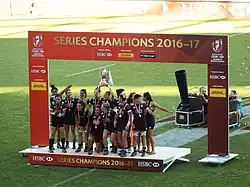 Joueuses sur un podium au centre du terrain, une joueuse tenant un trophée au dessus de sa tête.