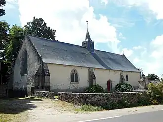 Vue d'une chapelle au toit d'ardoise, derrière un muret de pierres.