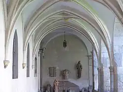 Photographie couleur montrant une aile de cloître, dans laquelle des objets archéologiques sont exposés.