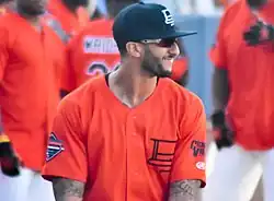Portrait d'un homme habillé d'un maillot de baseball orange, de lunettes de soleil et d'une casquette noire.