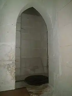 Photographie en couleurs d'une niche dans un mur et dont le sol est recouvert d'une grille.