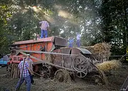Photographie en couleurs de personnages s'affairant autour de matériels agricoles.