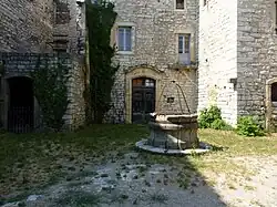 Coin d'une cour herbeuse, entourée d'un bâtiment de pierres. Le puits au centre est cerclé de fer.