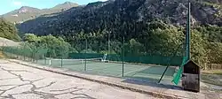 Photographie d'un court de tennis vert en contrebas de la montagne et protégé par des grillages verts.