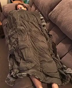 Une femme allongée sur un canapé, sous une couverture qui semble épaisse et qui la recouvre de son nez aux chevilles.