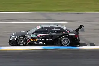 Voiture noire, de profil, sur une piste sèche.