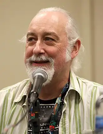 Photo en buste d'un homme, ayant un bouc et les cheveux blancs, et parlant dans un micro.