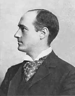 Photographie de profil et en noir et blanc d'un trentenaire en complet-veston arborant une mine sérieuse et un début de calvitie.